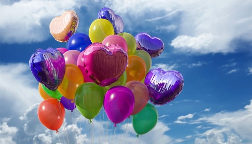 Bunte Luftballons fliegen vor einem blauen Himmel.